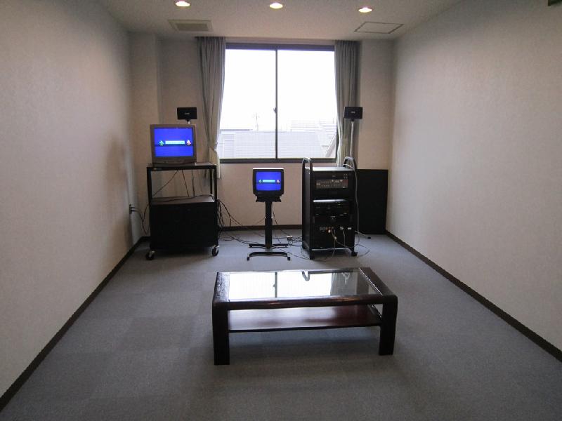 窓側にモニターが2台あり、その横に音響機材、手前には低いテーブルが置かれている音響室内の写真