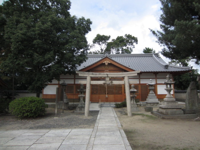 両端が樹木で覆われ中央に鳥居、白壁に木目のお社が見える、神社全体を写した写真