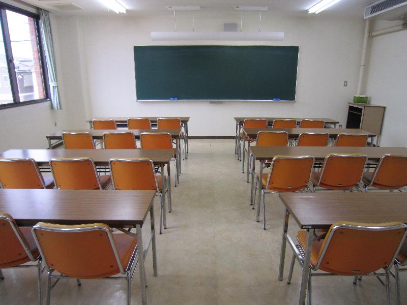 3脚ずつ椅子が置かれた長机が黒板の方向に2列に並べられている講座室3の写真