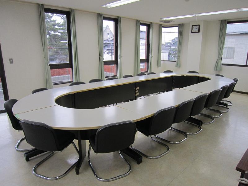 楕円形の形をした白いテーブルに椅子がきれいにセットされている小会議室の室内の写真