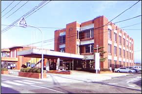 茶色の外観をした3階建ての建物で、玄関前に屋根付きのアプローチが設置されている田尻町役場庁舎全体を写した写真
