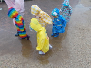 レインコートを着て水たまりの中を歩いている園児たちの写真