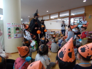 かぼちゃの国の魔女とくろねこに扮した先生とオレンジ色の三角帽子をかぶった園児たちの写真