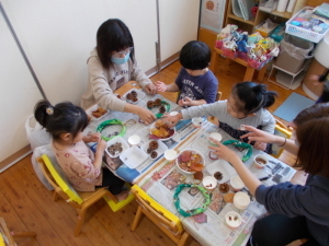 松ぼっくりや落ち葉などをボンドでリースに貼ってデコレーションしている園児たちの写真