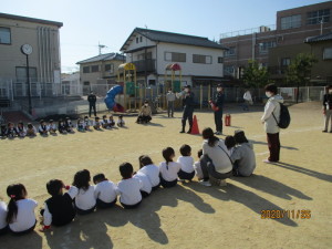 園庭に横一列に並んで座り、話を聞いている園児たちの写真