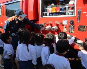 消防車の設備について説明している消防士と話を聞いている園児たちの写真