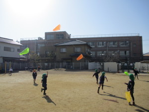 風を受けた凧を持ちながら一生懸命走っている園児たちの写真