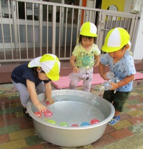 カラフルなボールが浮いているタライとペットボトルで水遊びしている3人の園児の写真