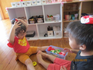 向かい合って座り、お手玉を頭の上に乗せて遊んでいる2人の園児の写真