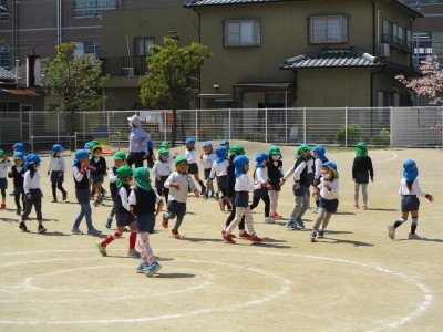 園庭に出ている青い帽子をかぶった園児と緑色の帽子をかぶった園児たちの写真