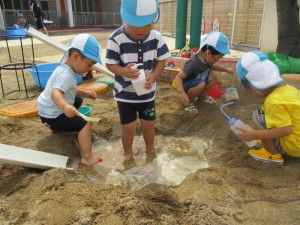砂場にできた水たまりで遊んでいる園児たちの写真