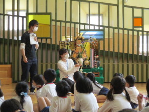 花瓶に生けられた菖蒲を見せている先生と座って見ている園児たちの写真