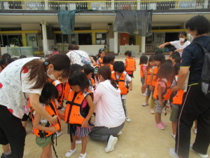 オレンジ色のライフジャケットを着て避難の準備をしている園児たちの写真