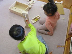 積み木の色々なパーツを高く積んで遊んでいる2人の園児の写真