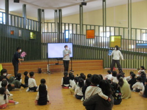 ペープサートをしている3人の先生と床に座って見ている園児たちの写真