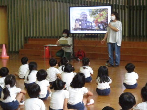 原爆ドームが映し出されたモニター画面を見ている園児たちとモニター横に立っている先生の写真