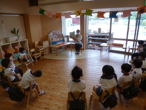 絵本の読み聞かせをしている先生と椅子に座って聞いている園児たちの写真