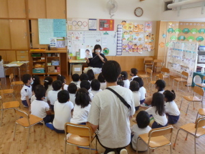 絵本の読み聞かせをしている先生と座って聞いている園児たちの写真
