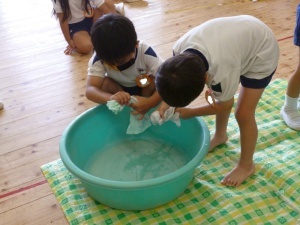 タライの中にタオルの水を絞っている園児たちの写真