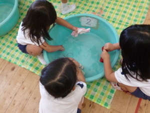 タオルを絞ってタライに溜まった水を見ている園児たちの写真