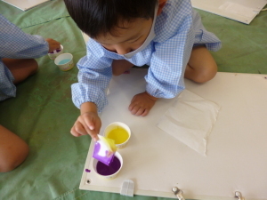紫色の絵の具に紙をつけている園児の写真
