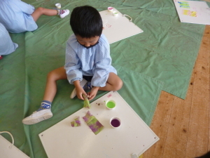 黄緑色と紫色の絵の具を使って紙に色をつけている園児の写真