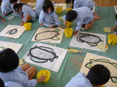 床に敷いたシートの上で絵の具を使ってトウモロコシの絵を書いている園児たちの写真