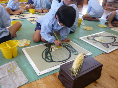 見本のトウモロコシを見ながら絵を書いている園児の写真