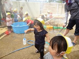 シャワーの放水で遊んでいる園児やタライの水で遊んでいる園児たちの写真